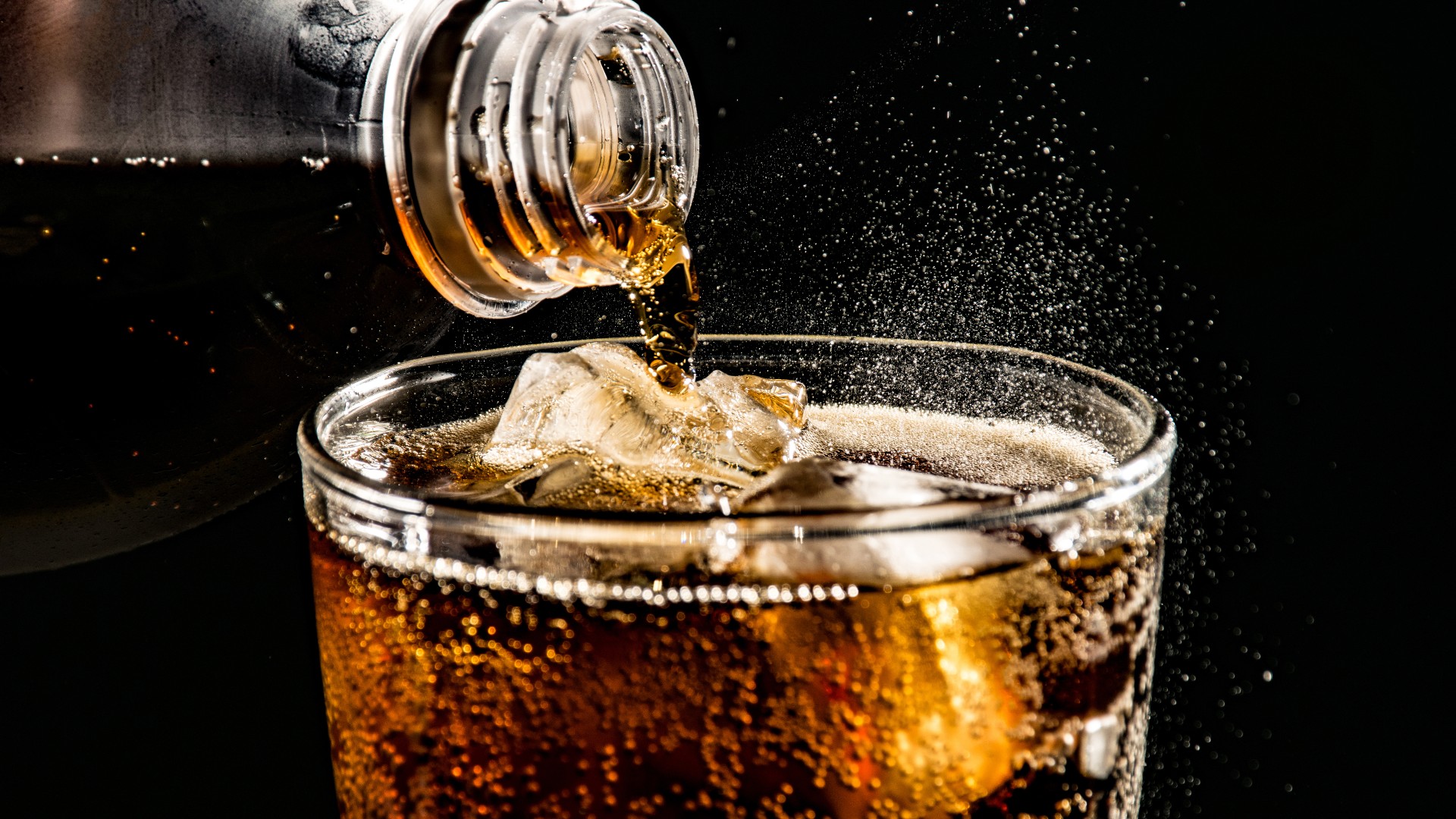 Gros plan de soda pétillant versé dans un verre à boire rempli de glace sur fond noir.