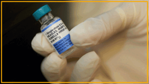 A close up of a glass bottle labeled measles vaccine being held by a gloved hand.