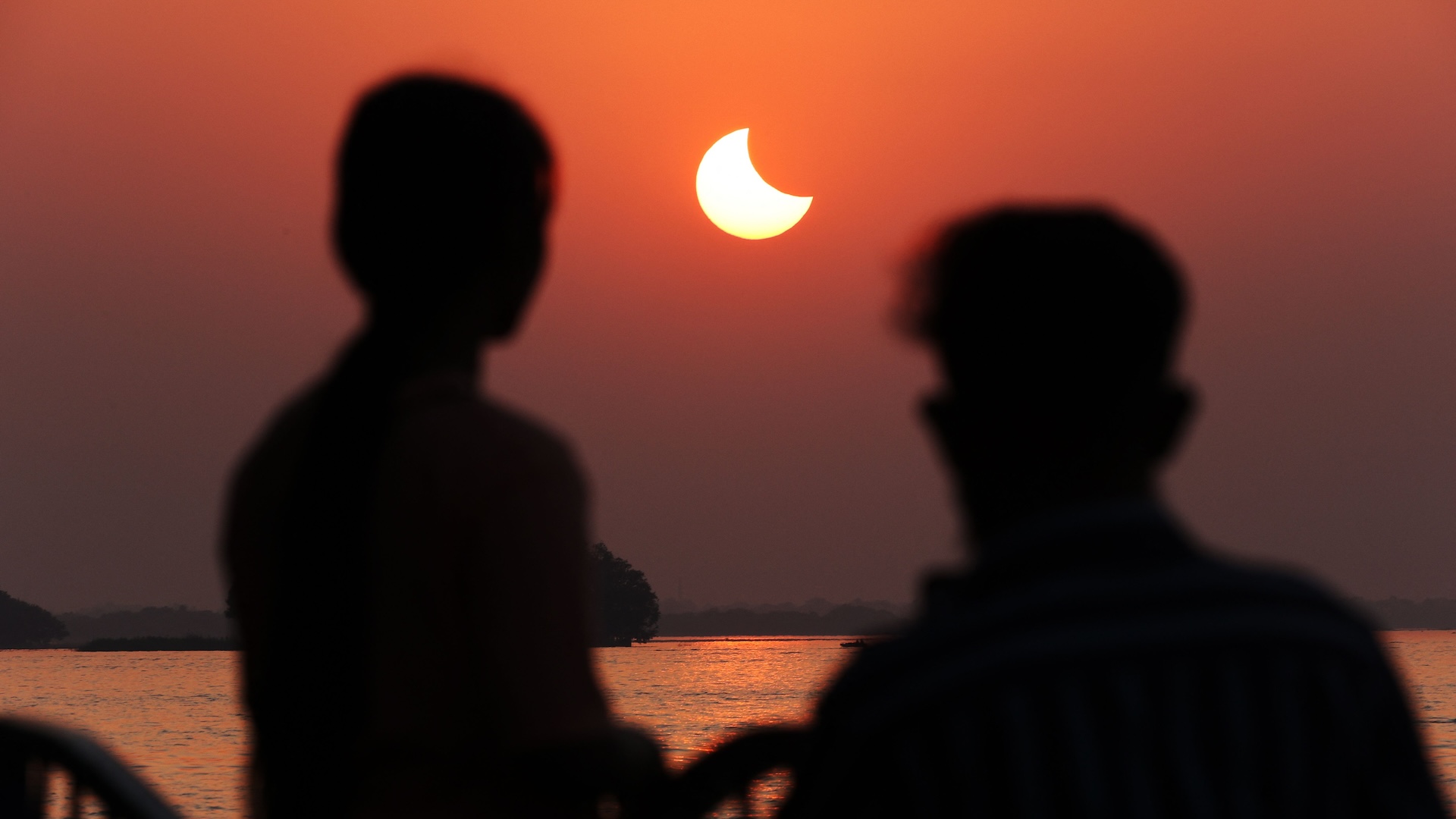 deux personnes regardent une éclipse solaire au lever du soleil
