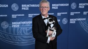 A man with gray hair wearing a black and white tuxedo holds a small black and white dog.