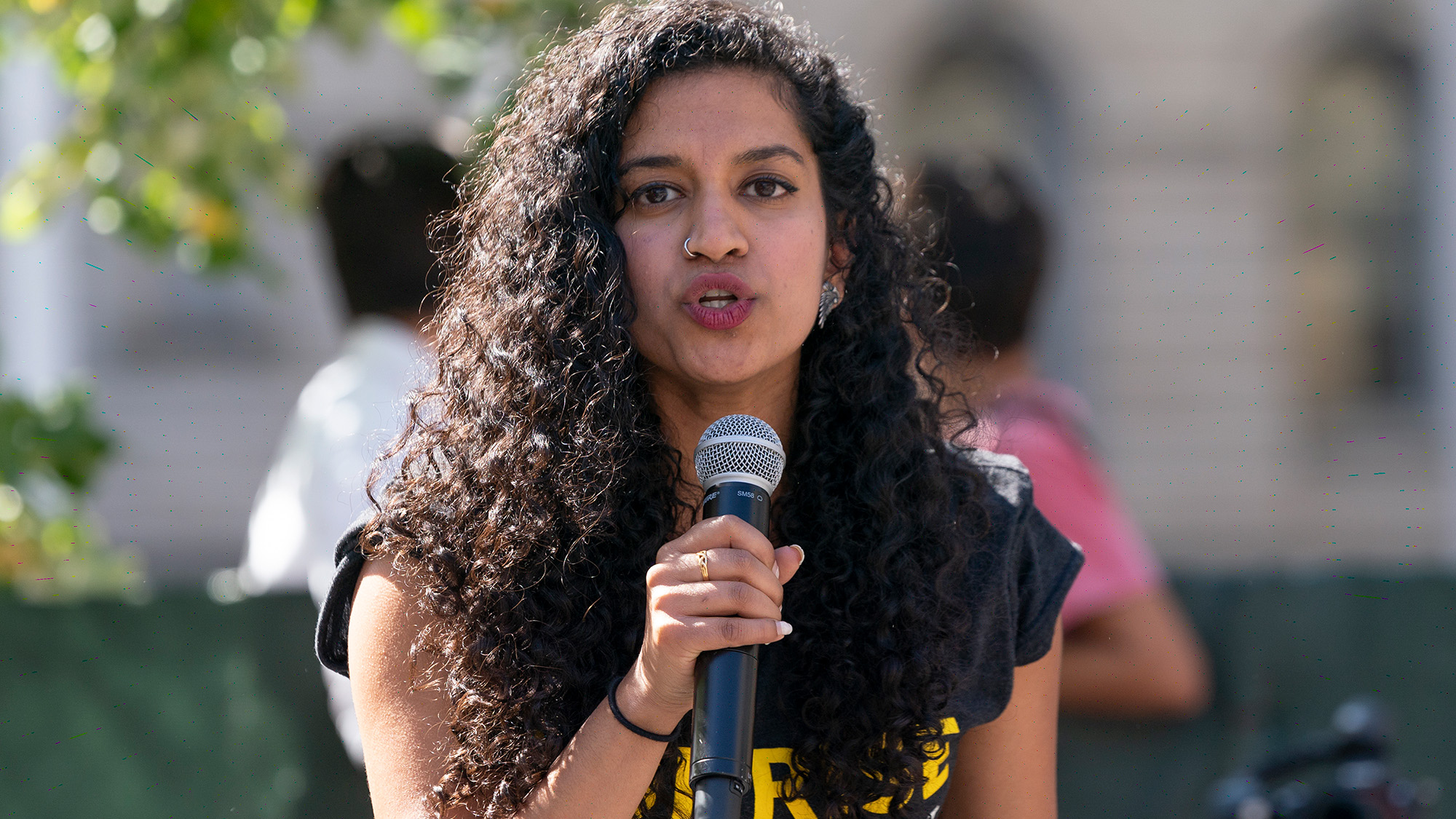 Une femme aux cheveux noirs et bouclés parle dans un microphone.