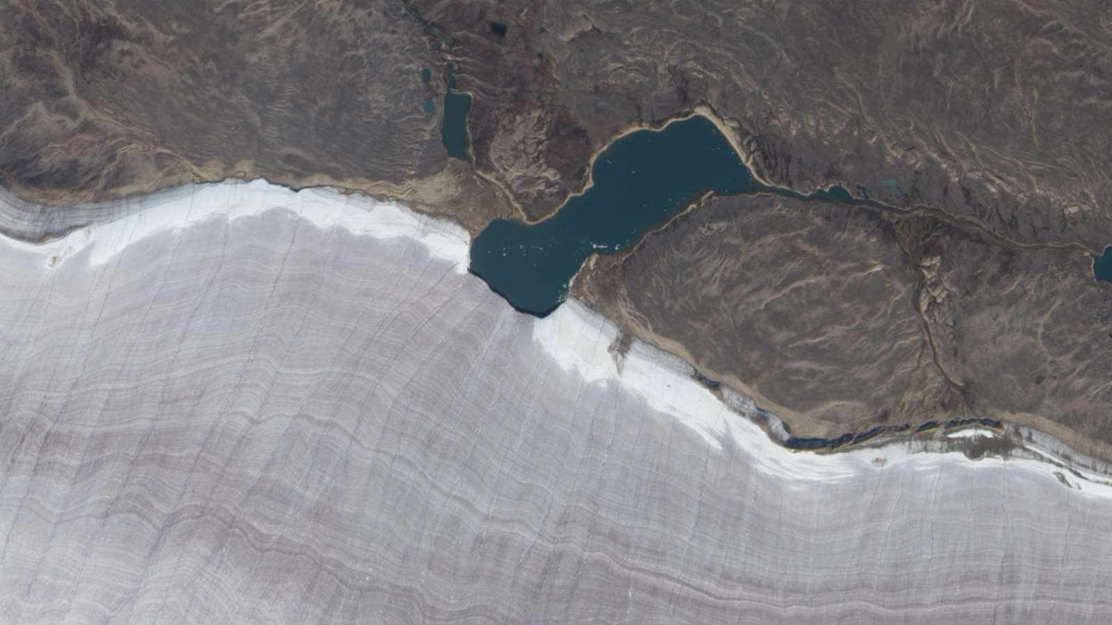 Photo satellite montrant un lac coupant en deux le bord enneigé d'un glacier à crêtes grises