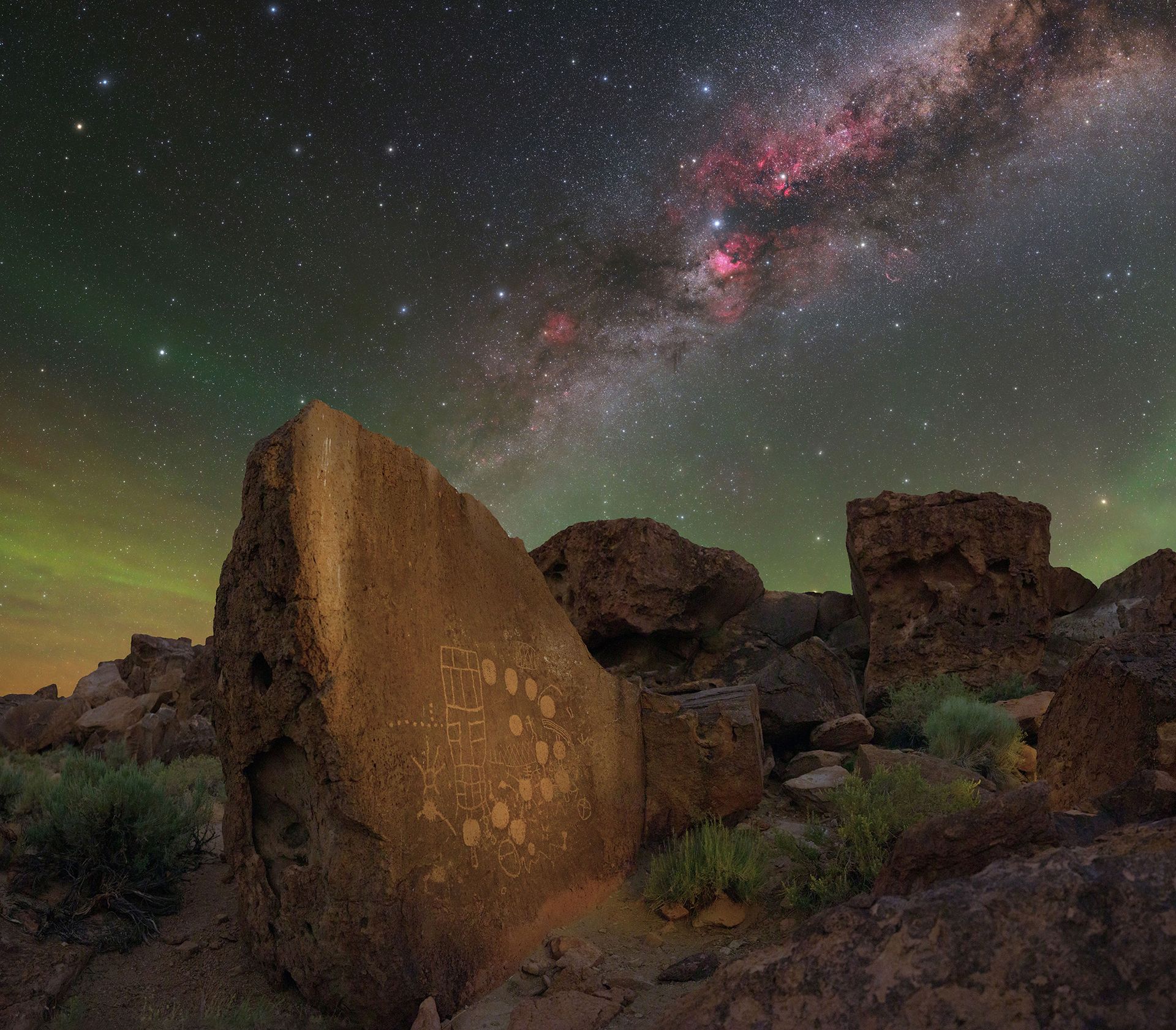Une galaxie rose est visible dans le ciel nocturne au-dessus d’une série de formations rocheuses.