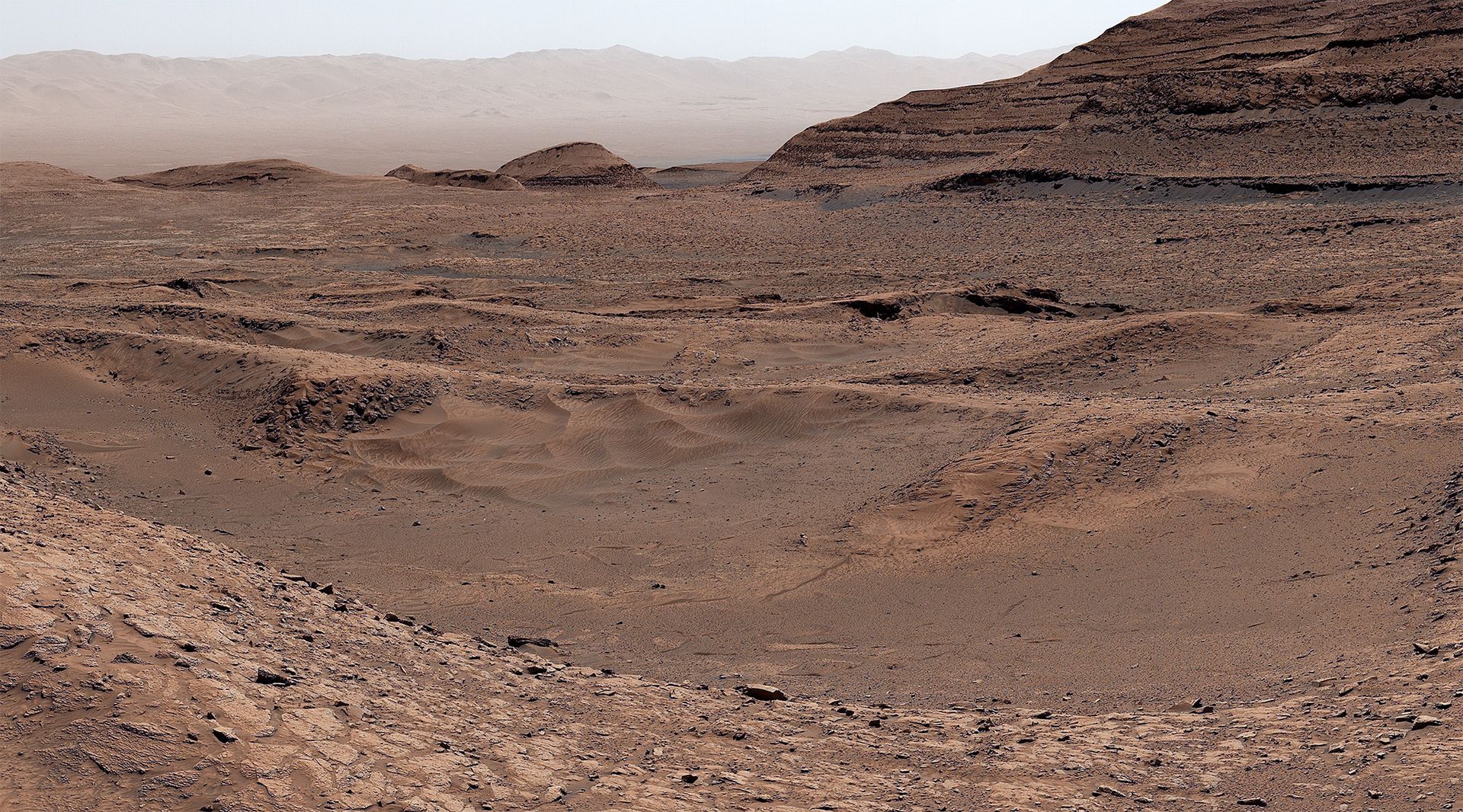 Un paysage brun rougeâtre avec des dunes au loin