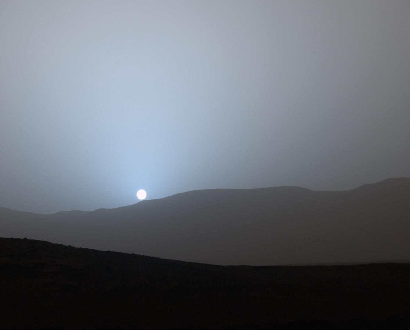 Une vue sur le coucher du soleil avec la silhouette d'une chaîne de montagnes en face.