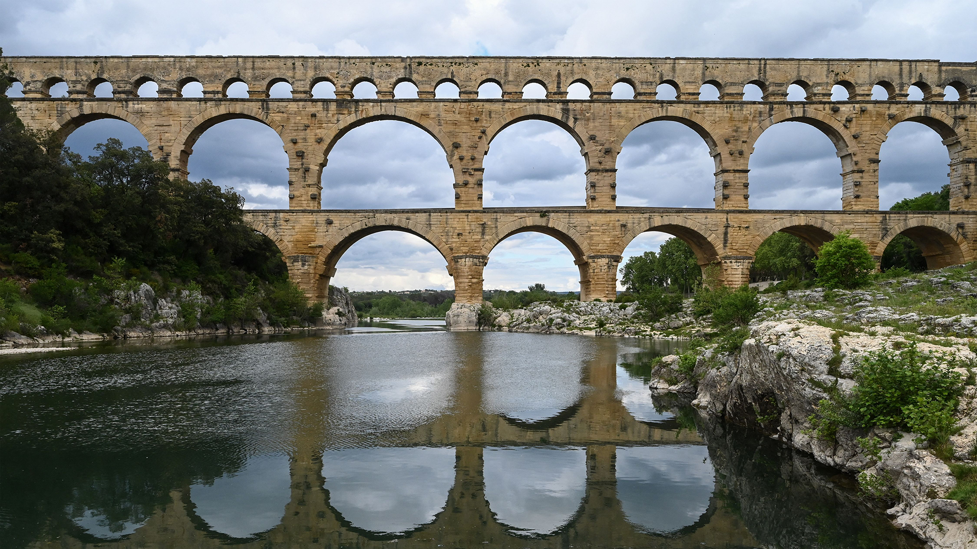 Un grand aqueduc en pierre est visible au-dessus d'une rivière.