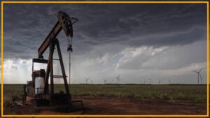 A close up of an oil rig with wind turbines in the background.