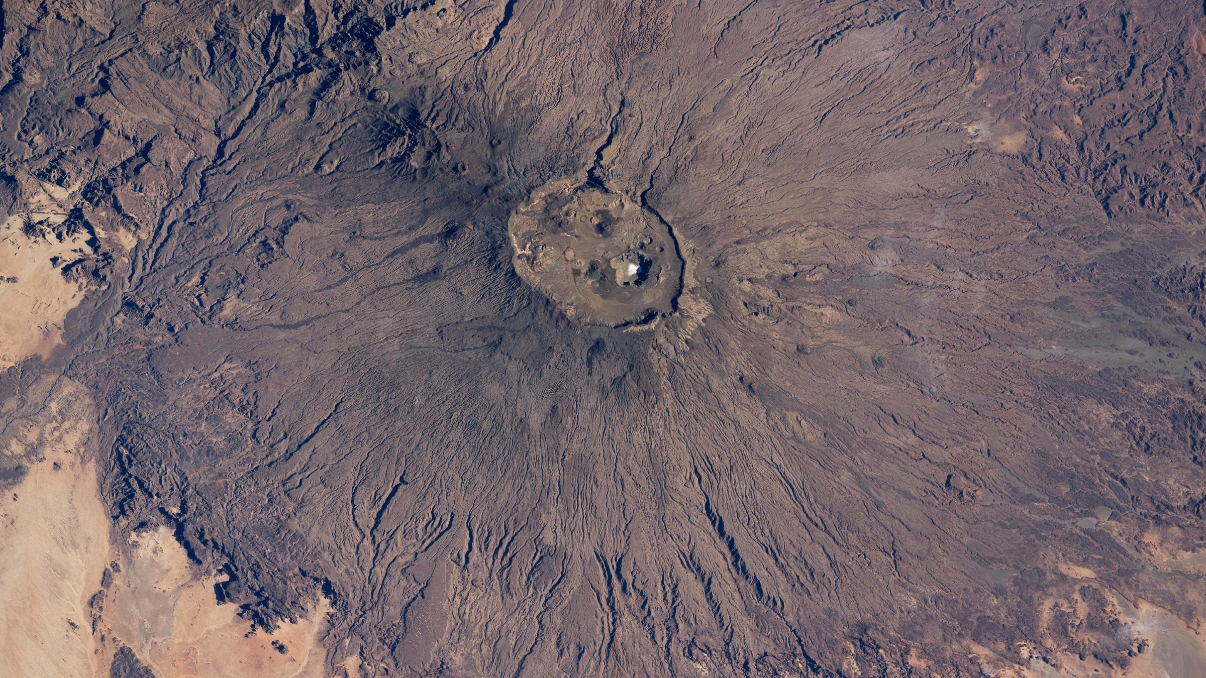 Photo satellite d'un volcan dans le désert du Sahara avec une tache blanche brillante à son sommet