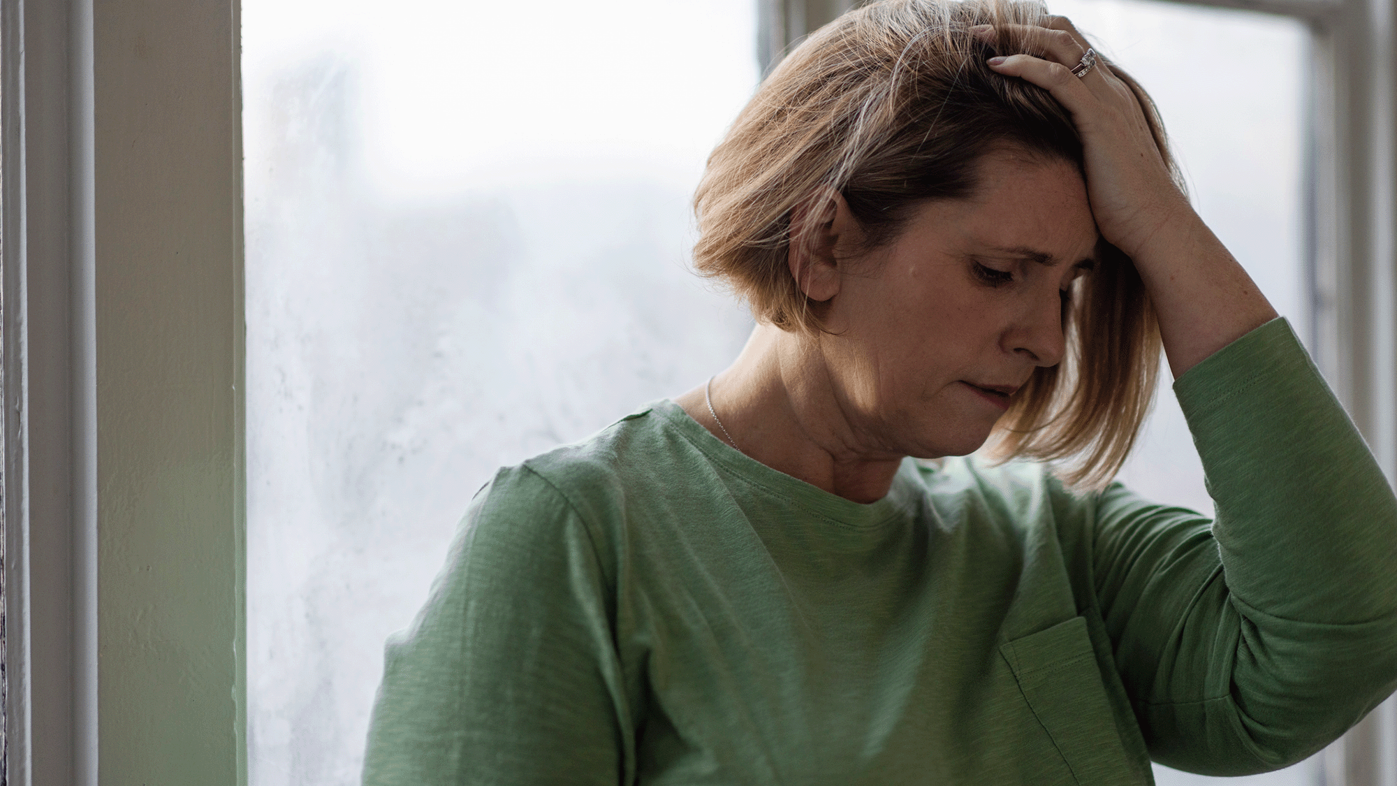 A woman wearing a green sweater holds her head in her hands.