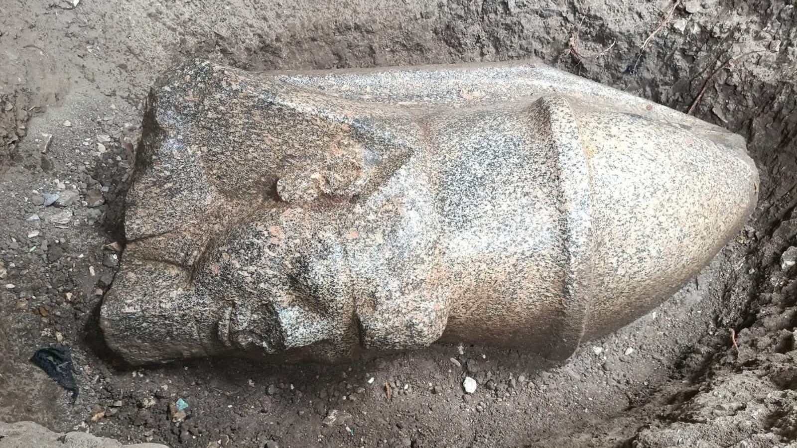 The head of a statue lying horizontally on the ground. It shows a man wearing a pointy hat.