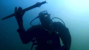 an underwater photograph shows a person wearing a dive suit holding a Bronze Age sword
